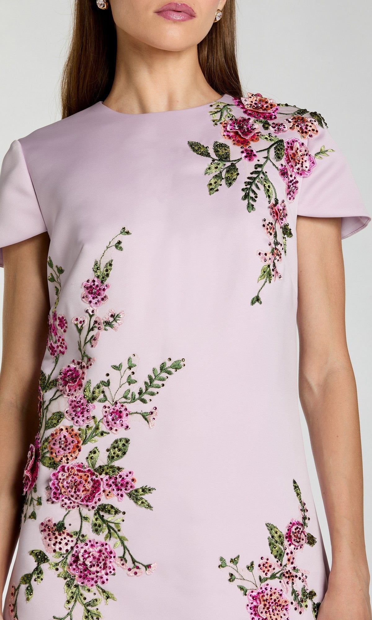 A woman wearing the Mac Duggal 21338 short wedding guest dress, featuring light pink short sleeves and elegant pink and green floral embroidery on the upper chest and side.
